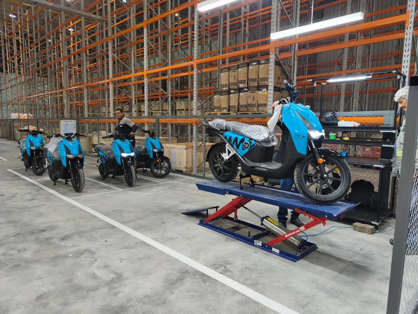 Motos elétricas Vammo enfileiradas na nova unidade, com elevador de preparo à direita